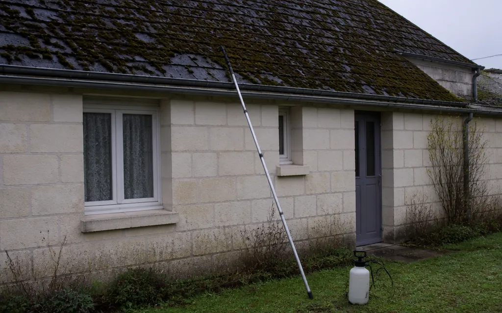 Perche télescopique et pulvérisateur de jardin posés au pied d’une maison, le toit hors de portée au-dessus